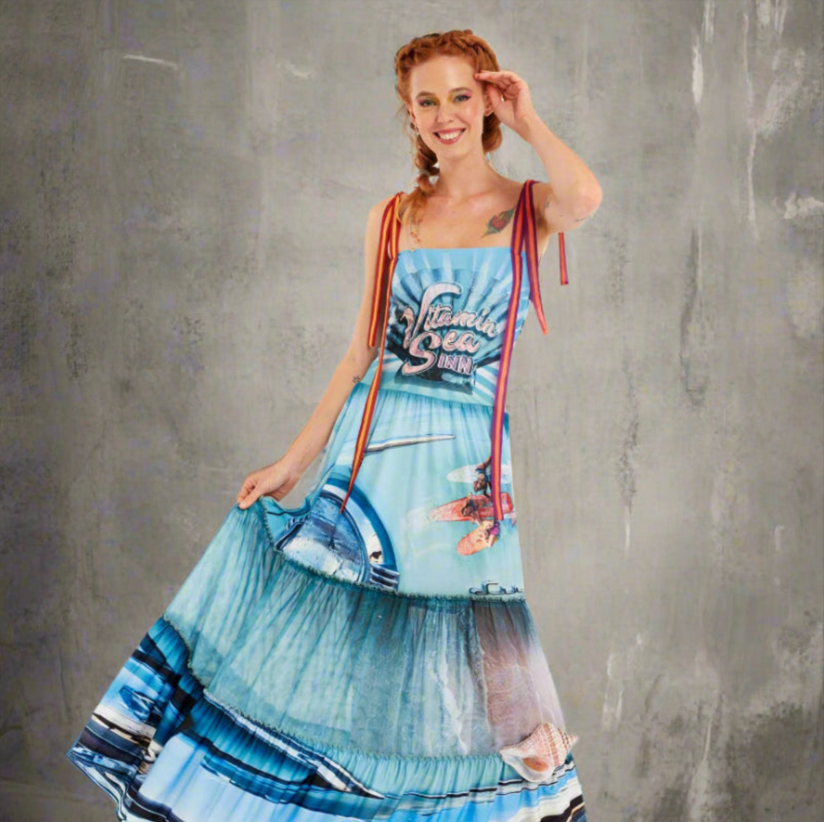 Woman wearing a convertible maxi dress with vibrant ocean print, tie straps, and rhinestone details; worn as a dress with peek-a-boo panel.