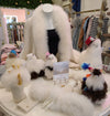 A display of alpaca-themed items, including plush toy llamas, alpaca wool mittens, a fur-trimmed shawl, and slippers, arranged on a boutique table.