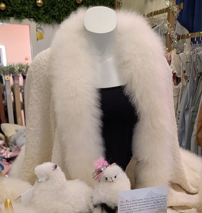 A cream-colored alpaca wool shawl with a plush fur trim, displayed on a mannequin in a boutique setting.


