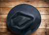 A black vegan suede cowboy hat with a flat brim and arrowhead crease, displayed on a wooden table