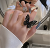 Close-up of a black rhinestone butterfly adjustable ring on a woman's hand, reflecting in a mirror.