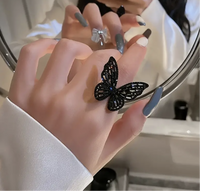 Close-up of a black rhinestone butterfly adjustable ring on a woman's hand, reflecting in a mirror.