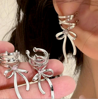 Close-up of a woman wearing a silver bow dangle cuff earring, featuring a lace-up cuff design and sparkling rhinestone accent, with an elegant, modern style.