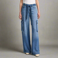 Close-up of high-waisted blue denim palazzo jeans with utility-style cargo pockets and a matching denim tie belt, styled with a white tank and cream heels