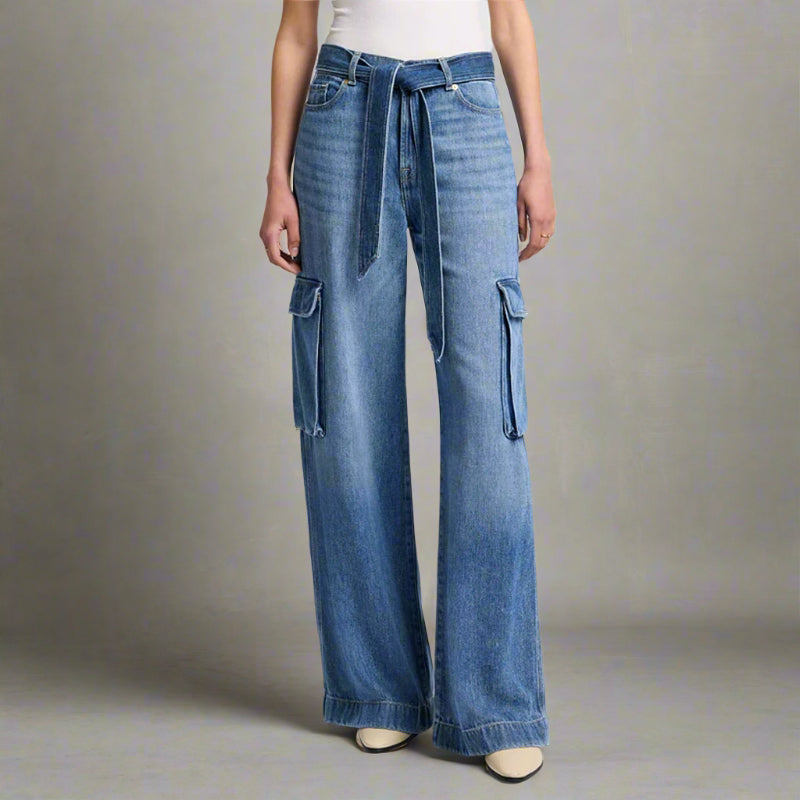 Close-up of high-waisted blue denim palazzo jeans with utility-style cargo pockets and a matching denim tie belt, styled with a white tank and cream heels