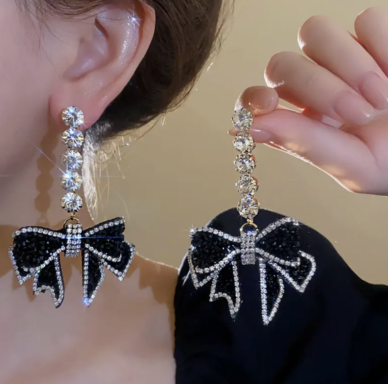 A pair of black crystal-studded bow earrings with cascading rhinestone accents, designed for a glamorous and elegant look.