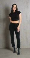 Woman wearing black rhinestone-studded demi bootcut jeans with raw frayed hems, styled with a black crop top and boots