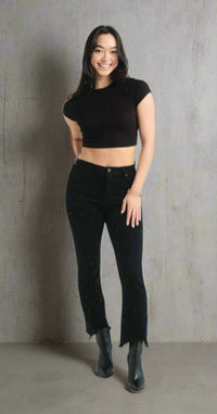 Woman wearing black rhinestone-studded demi bootcut jeans with raw frayed hems, styled with a black crop top and boots