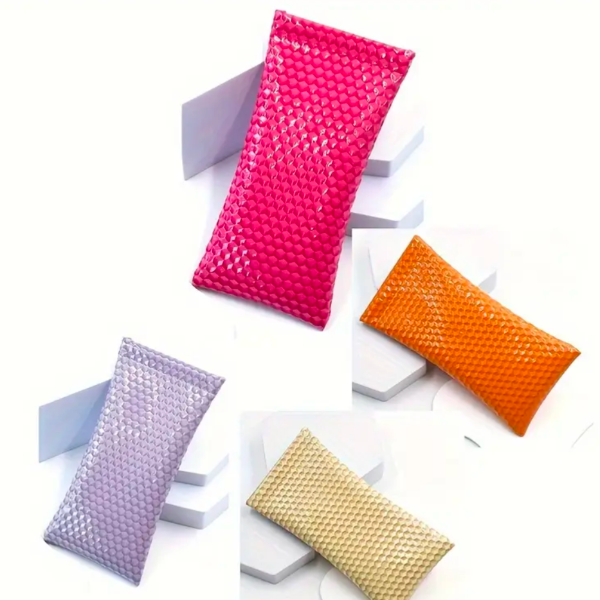 Assorted glossy sunglass cases in pink, lilac, orange, and champagne with embossed square texture displayed on geometric white platforms.