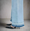 Close-up of frayed raw hem and seam detail on light blue wide-leg jeans, styled with black pointed heels
