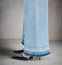 Close-up of frayed raw hem and seam detail on light blue wide-leg jeans, styled with black pointed heels