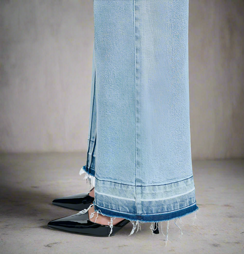 Close-up of frayed raw hem and seam detail on light blue wide-leg jeans, styled with black pointed heels