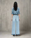 Woman wearing light blue wide-leg jeans with single back seam stitching, raw hems, and a black belt