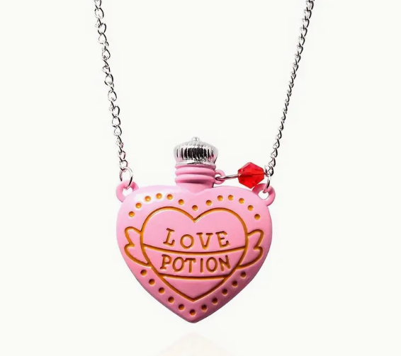 A pink heart-shaped potion bottle pendant with gold detailing, "Love Potion" engraving, a silver-tone cap, and a small red crystal charm on a delicate chain.