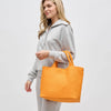 Model carrying a medium woven neoprene tote in a warm neutral tone, featuring a chic, textured design with sturdy woven handles.