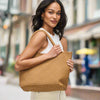 Model carrying a medium woven neoprene tote in a warm neutral tone, featuring a chic, textured design with sturdy woven handles.

