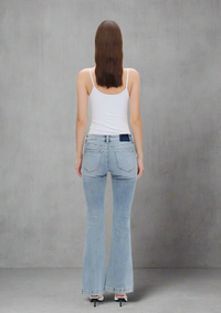 Back view of light wash low-rise flare jeans with finished hems, styled with a white tank top and heels