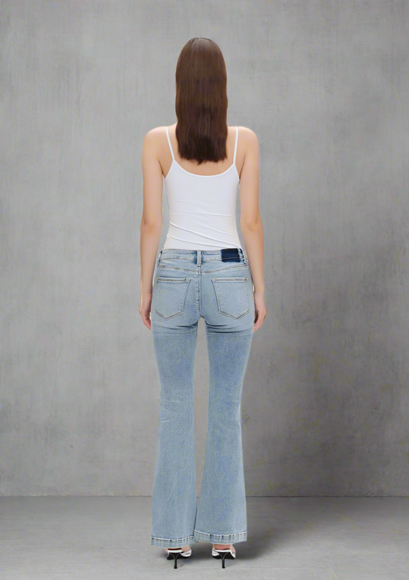 Back view of light wash low-rise flare jeans with finished hems, styled with a white tank top and heels