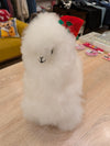 A fluffy white alpaca plush toy standing on a wooden surface in a boutique setting.