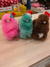 A set of three fluffy alpaca plush toys in pink, green, and brown, made from soft alpaca wool, standing on a wooden surface.

