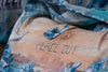 Close-up of linen tote bag pocket with “Peace Out” text, peace sign graphic, and blue floral strap with button closure