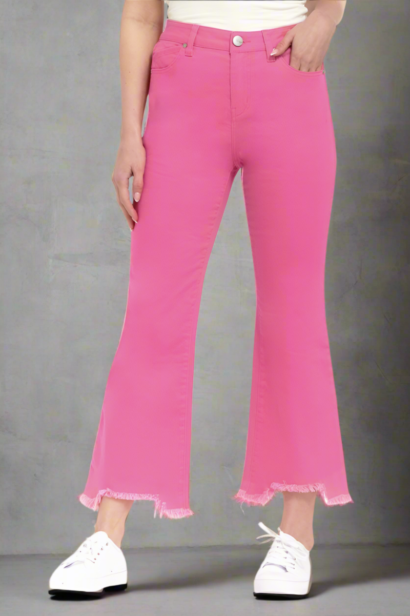 Woman wearing hot pink high-rise bootcut jeans with frayed shark bite hems, paired with white sneakers and tank