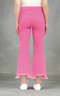 Woman wearing hot pink high-rise bootcut jeans with frayed shark bite hems, paired with white sneakers and tank