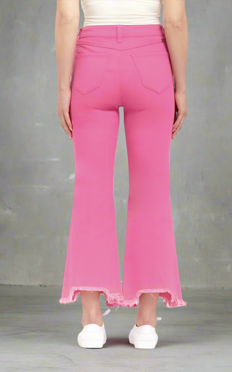 Woman wearing hot pink high-rise bootcut jeans with frayed shark bite hems, paired with white sneakers and tank
