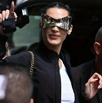 Woman wearing oversized mirrored gradient sunglasses with a futuristic wraparound shape, holding a camera while dressed in black.

