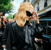 Woman wearing oversized mirrored gradient sunglasses with a futuristic wraparound shape, holding a camera while dressed in black