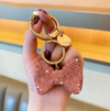A dazzling rhinestone-encrusted bow keychain with gold-tone brass hardware, featuring a sturdy clasp and keyring, designed as a stylish purse charm or bag accessory.