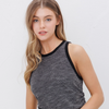 Woman wearing a charcoal ruched tank top with black trim and denim shorts, standing against a white wall.