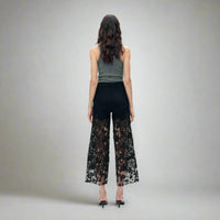 Back view of black high-rise jeans with sheer lace paneling from thigh to hem, styled with a grey tank top and heels