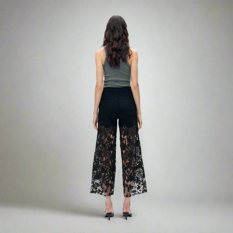 Back view of black high-rise jeans with sheer lace paneling from thigh to hem, styled with a grey tank top and heels