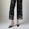 Close-up view of black lace cutout detailing on wide-leg jeans with floral patterns and nude lining, paired with black pointed heels.