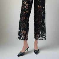Close-up view of black lace cutout detailing on wide-leg jeans with floral patterns and nude lining, paired with black pointed heels.