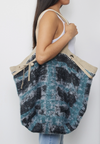Reversible slouchy canvas tote bag made from recycled coffee bean bags, featuring a fuzzy navy plaid interior, oversized grommets, adjustable drawstring closure, and webbing strap handles. Includes a small zip-up pouch.