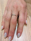A thin sterling silver hammered ring worn on a hand, resting on a wooden surface.