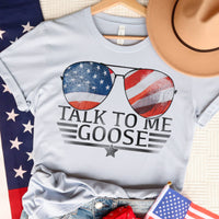 Light blue graphic t-shirt featuring aviator sunglasses with an American flag design and "Talk to Me Goose" text in bold, vintage-style print.