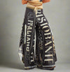 Black wide-leg pants with vintage Italian restaurant text print and rhinestone embellishments, styled with neutral wrap top