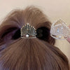 A rhinestone high ponytail clip in a tiara-inspired design, secured on a brunette ponytail, with sparkling crystals and pearl accents, available in gold and silver finishes.

