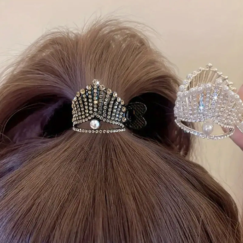 A rhinestone high ponytail clip in a tiara-inspired design, secured on a brunette ponytail, with sparkling crystals and pearl accents, available in gold and silver finishes.

