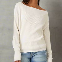 Model wearing a taupe waffle-knit slouchy sweater styled off one shoulder, paired with light denim jeans against a grey background.

