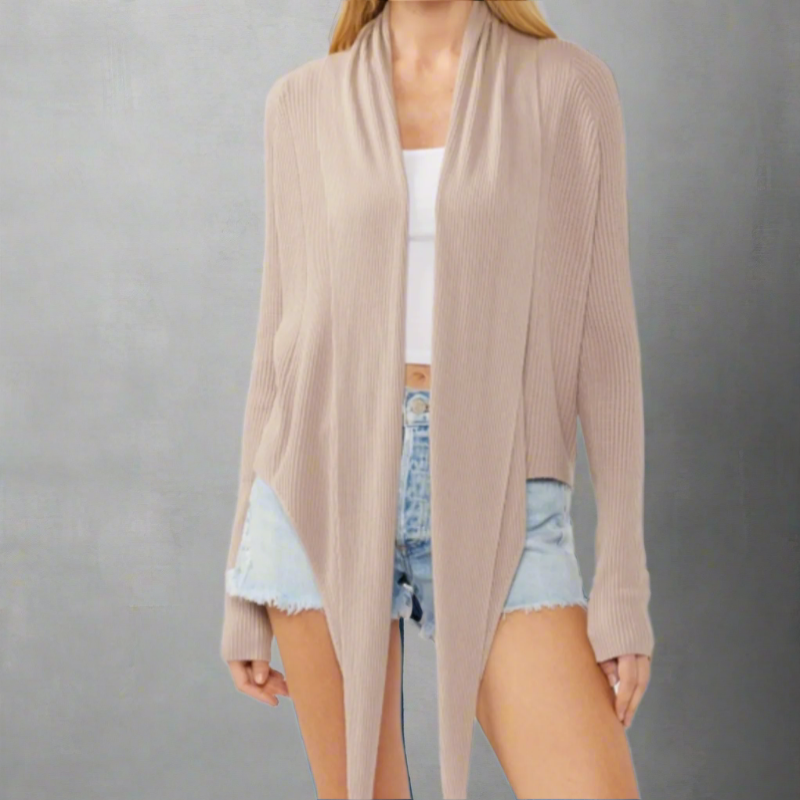 Woman wearing a taupe waffle knit cardigan with a long, draped front over a white tank top and denim shorts.