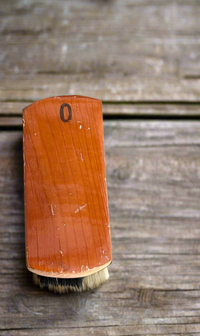 A wooden horsehair hat brush with a classic finish, featuring soft bristles, resting on a rustic wooden surface.