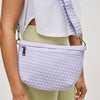 Model wearing a woven neoprene crossbody bag in a soft pastel shade, featuring an adjustable strap, zipper closure, and modern gunmetal hardware.