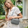 A woman in a white button-down dress wearing a sleek gray woven neoprene crossbody bag with an adjustable strap, styled for a casual yet chic look.