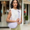 Model wearing a woven neoprene crossbody bag in a soft pastel shade, featuring an adjustable strap, zipper closure, and modern gunmetal hardware.

