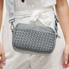 A sleek gray woven neoprene crossbody bag with an adjustable strap, styled for a casual yet chic look.

