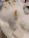 A pair of alpaca wool fingerless gloves with a fluffy fur trim, displayed on a boutique table.